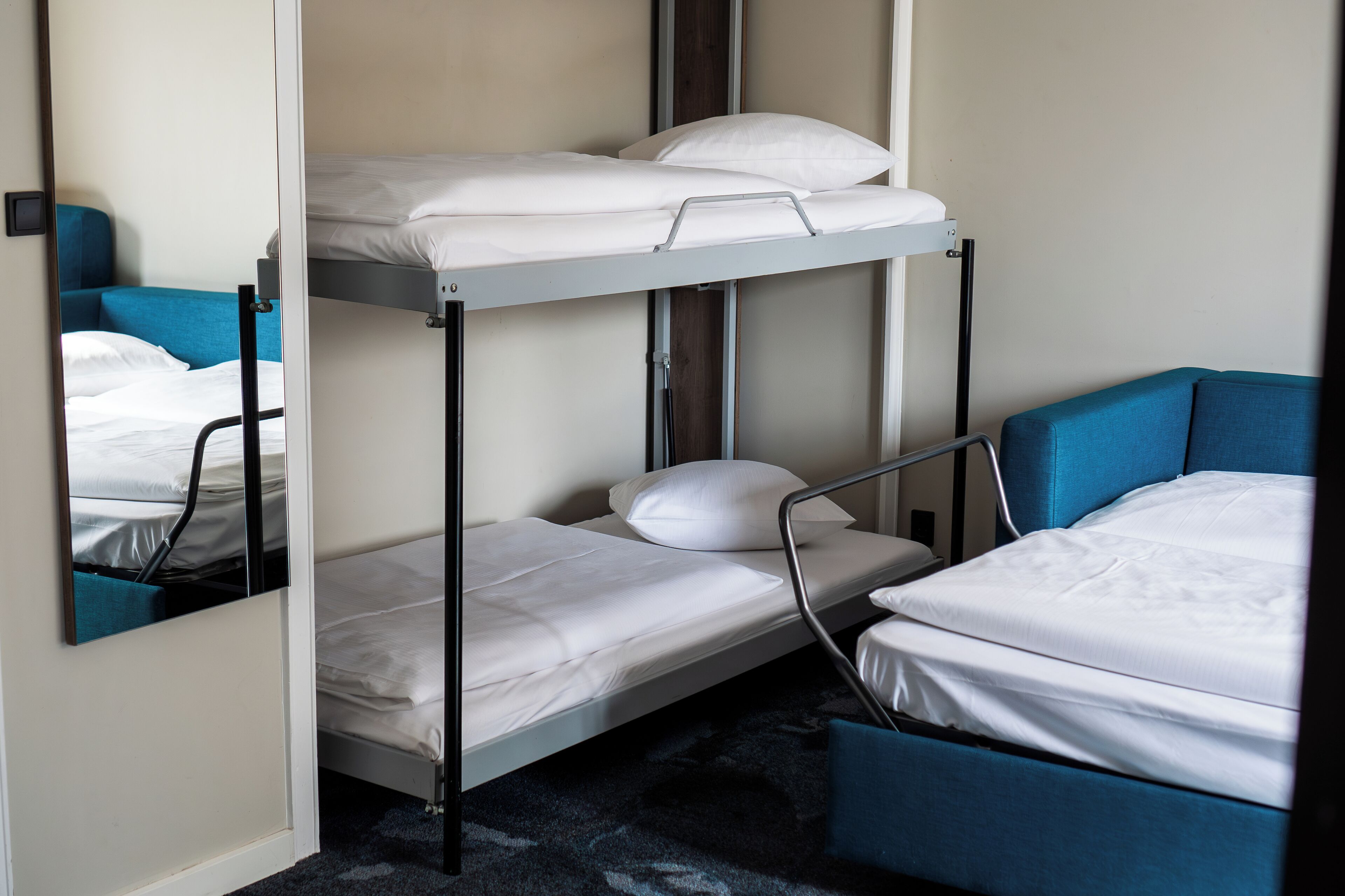 A bunk bed room with a mirror reflecting the bed and a blue chair.
