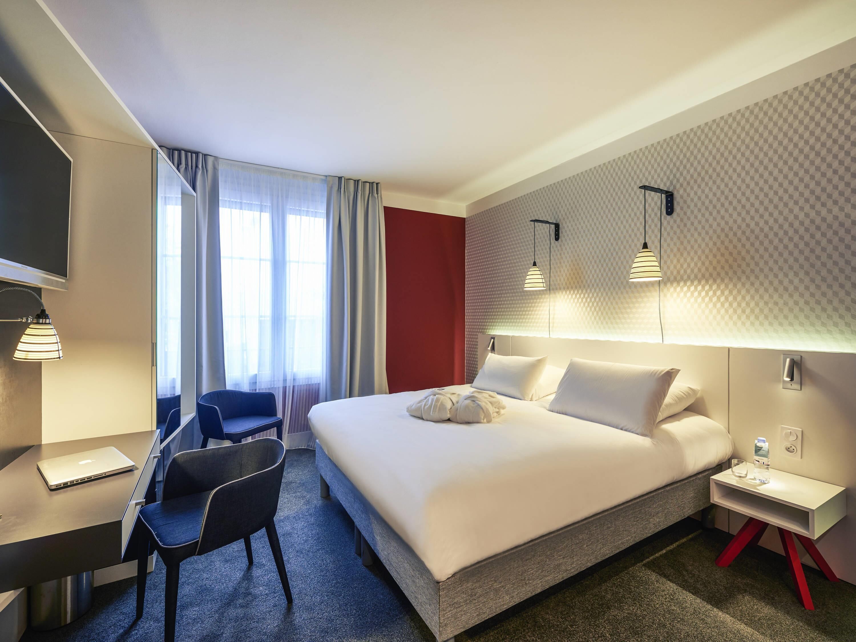 A modern hotel room with a bed, desk, chair, and a TV.