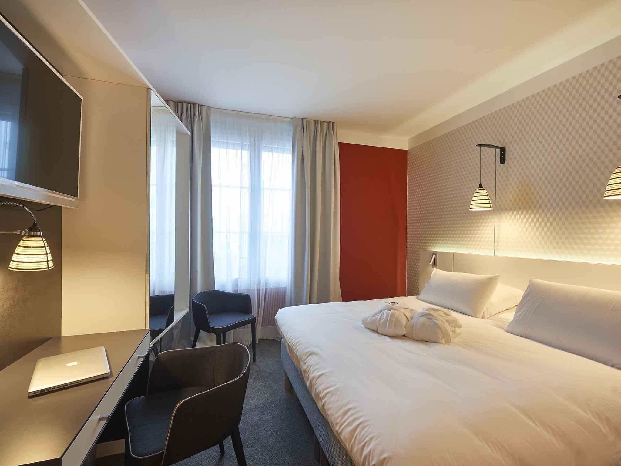 A hotel room with a bed, a desk, a chair, a TV, and a window with curtains.