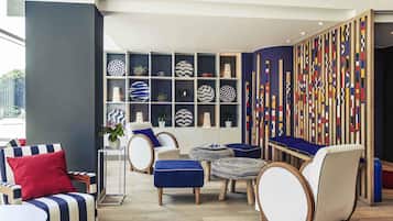 Relax in our stylish lobby, featuring a seating area with armchairs and ottomans, decorative shelves, and a vibrant geometric wall panel.