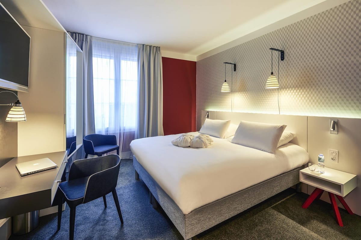 Habitación de hotel con cama, escritorio, silla y televisión.