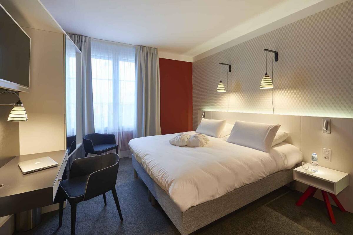 Habitación de hotel con cama, escritorio, silla y televisor.