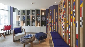 Un salon moderne comprenant un canapé, un fauteuil, un pouf et un mur décoratif orné de motifs géométriques.