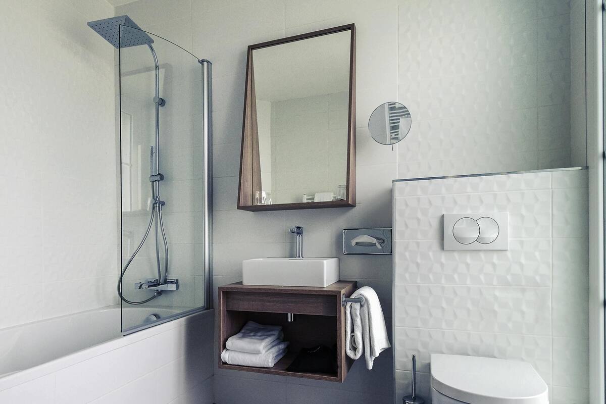 Un baño moderno con ducha envuelta en vidrio, tocador de madera con lavamanos y un inodoro con bidé integrado en la pared.