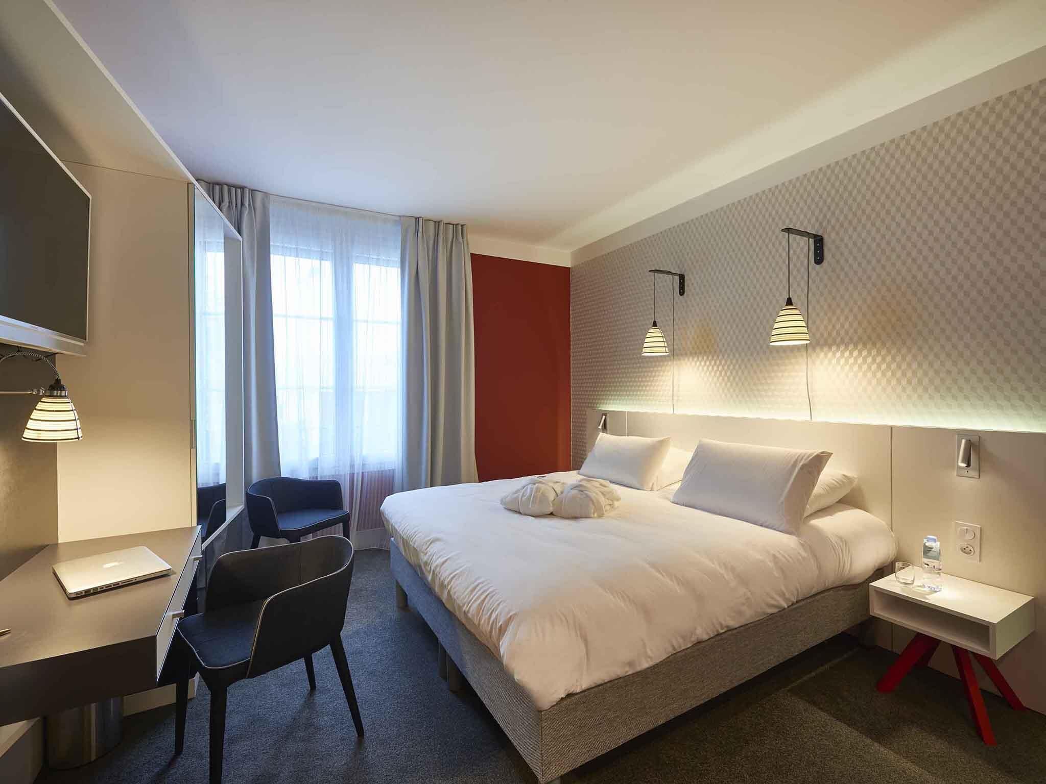 Habitación de hotel con cama, escritorio, silla y televisor.