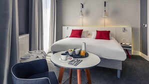Une chambre d’hôtel comprenant un lit, une table de chevet, une chaise et une petite table ronde avec des éléments pour le petit-déjeuner.