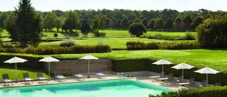A swimming pool with lounge chairs and umbrellas, surrounded by well-maintained lawns and trees.