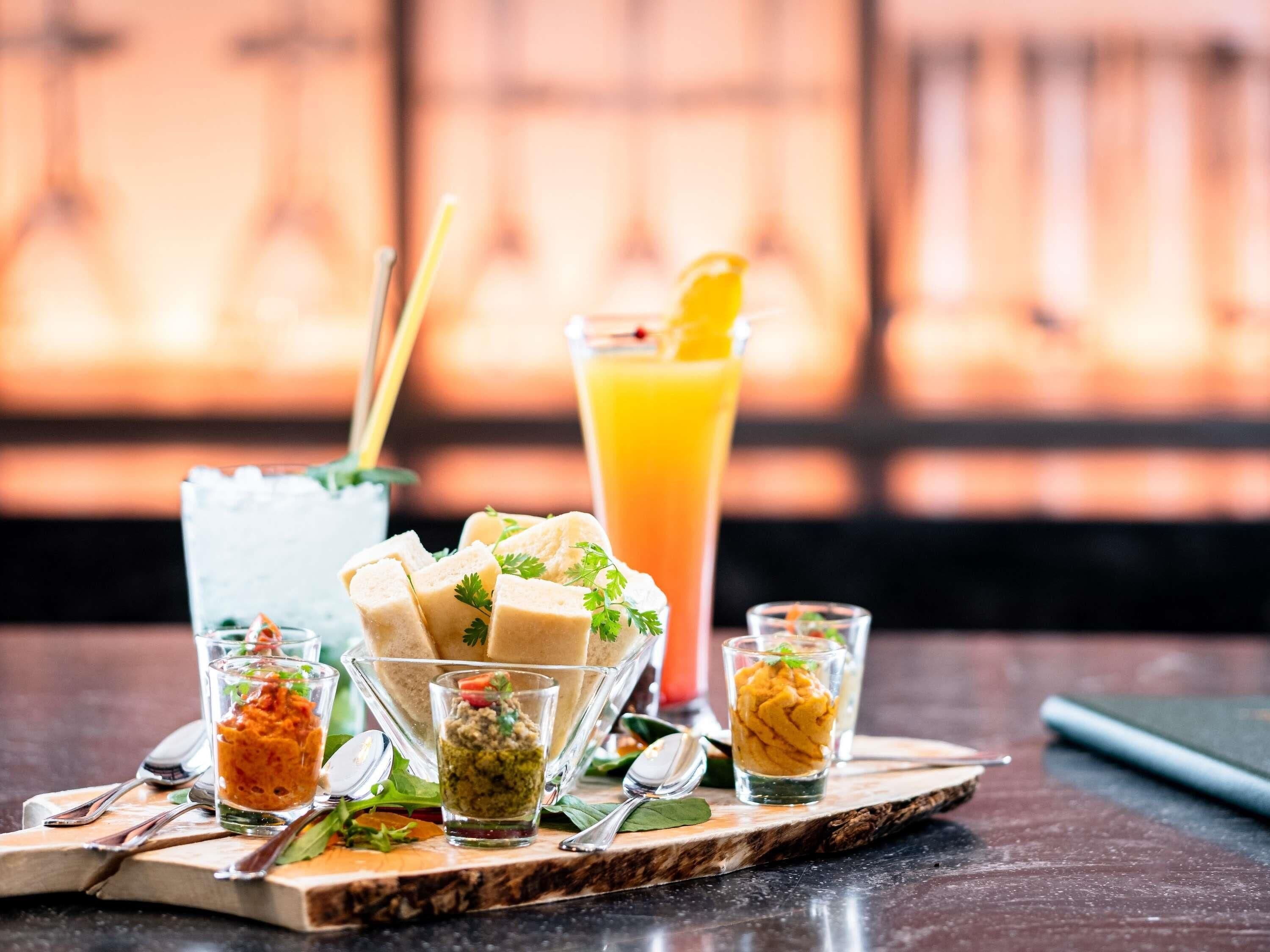 A table with various food items and drinks, including a tall glass of orange juice and several small glasses containing different sauces or dips.