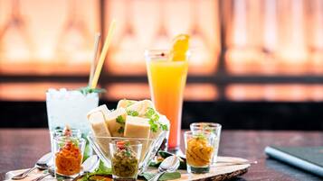 A table with various food items and drinks, including a tall glass of orange juice and several small glasses containing different sauces or dips.