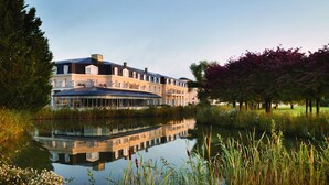 A large, multi-story building with a reflective pool in front, surrounded by lush greenery and trees. - Mercure Chantilly Resort & Conventions (Vineuil-Saint-Firmin)
