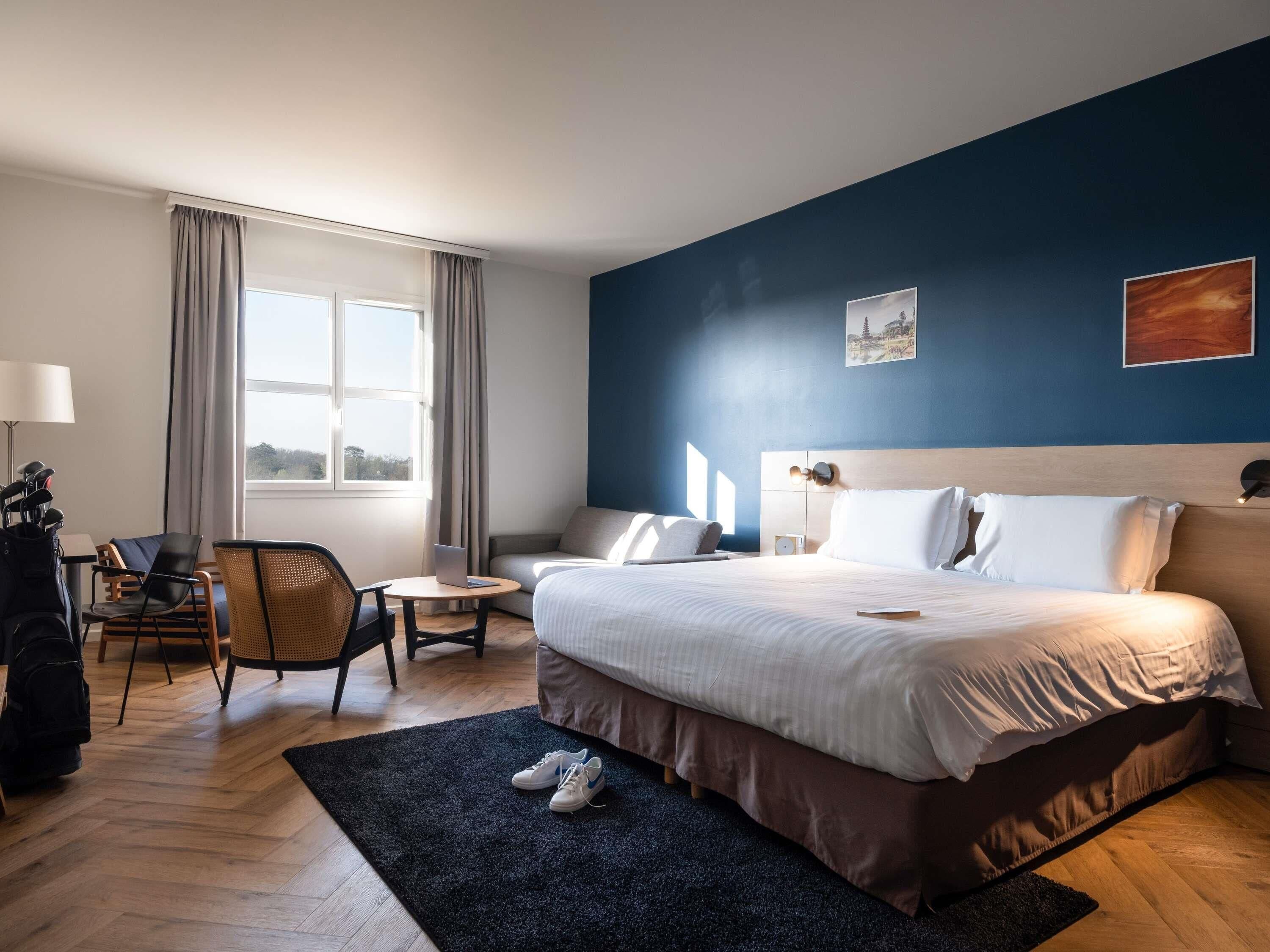 Habitación de hotel con cama, escritorio, silla, ventana y vistas al exterior.