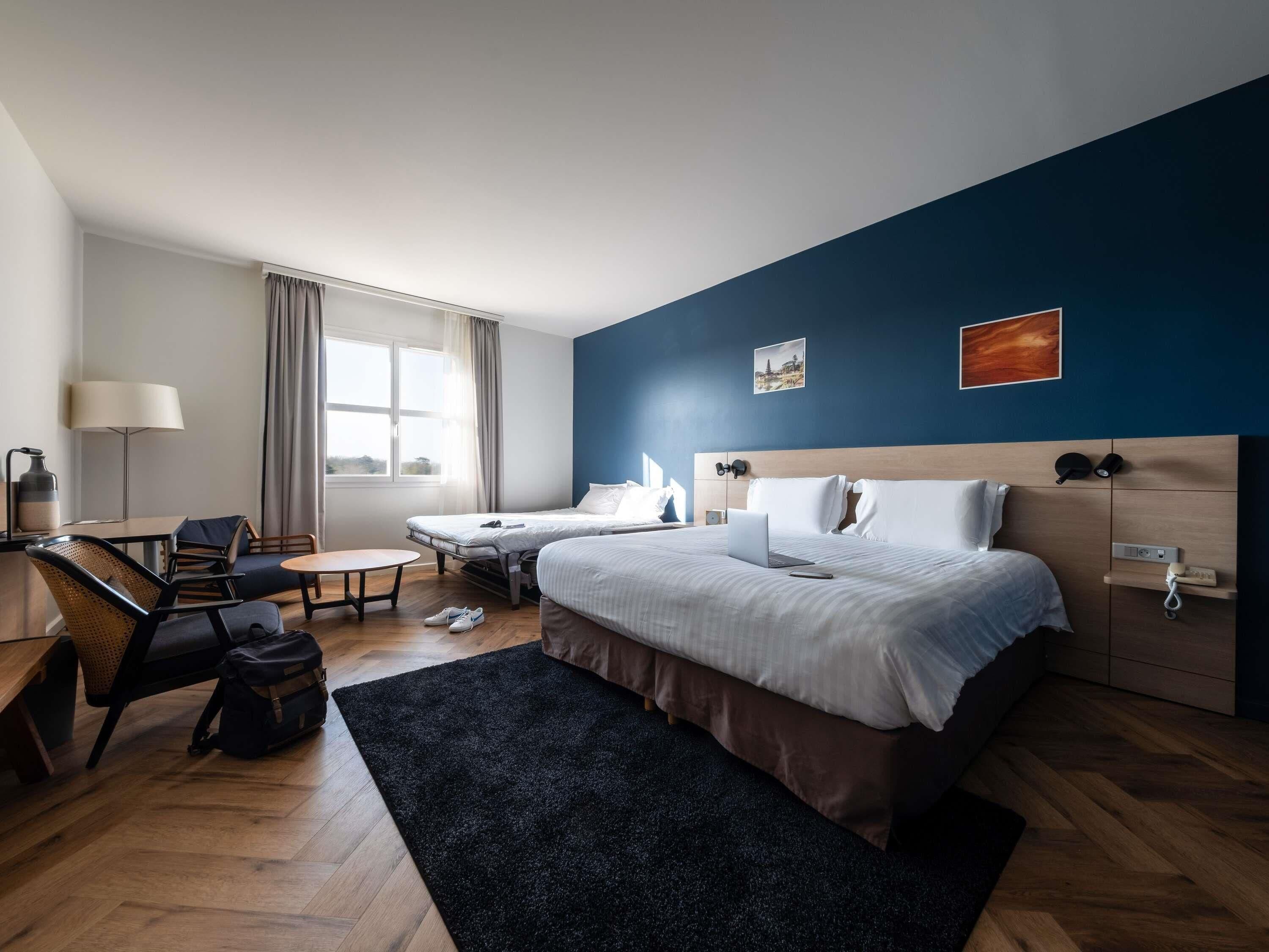 Habitación de hotel con una cama, un escritorio, una silla, una computadora portátil y una ventana.
