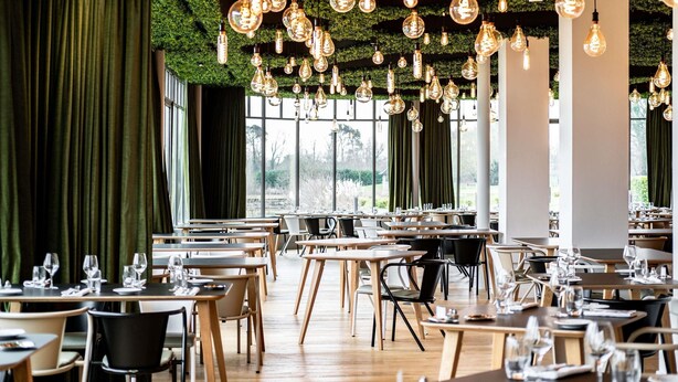 A restaurant with tables and chairs, hanging light bulbs, and a green curtain. - Mercure Chantilly Resort & Conventions (Vineuil-Saint-Firmin)