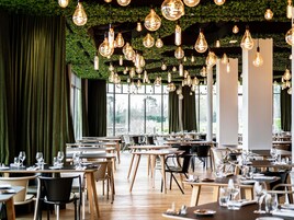 Un restaurante con mesas y sillas, bombillas colgantes y una cortina verde.