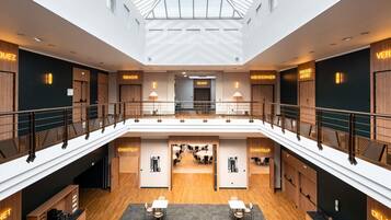 Un atrium d’hôtel moderne avec un plafond en verre, de nombreux étages et différents restaurants portant des noms tels que « RENOIR » et « CHANTILLY ».