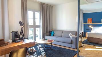 A hotel room with a desk, sofa, and a large mirror reflecting the bed.