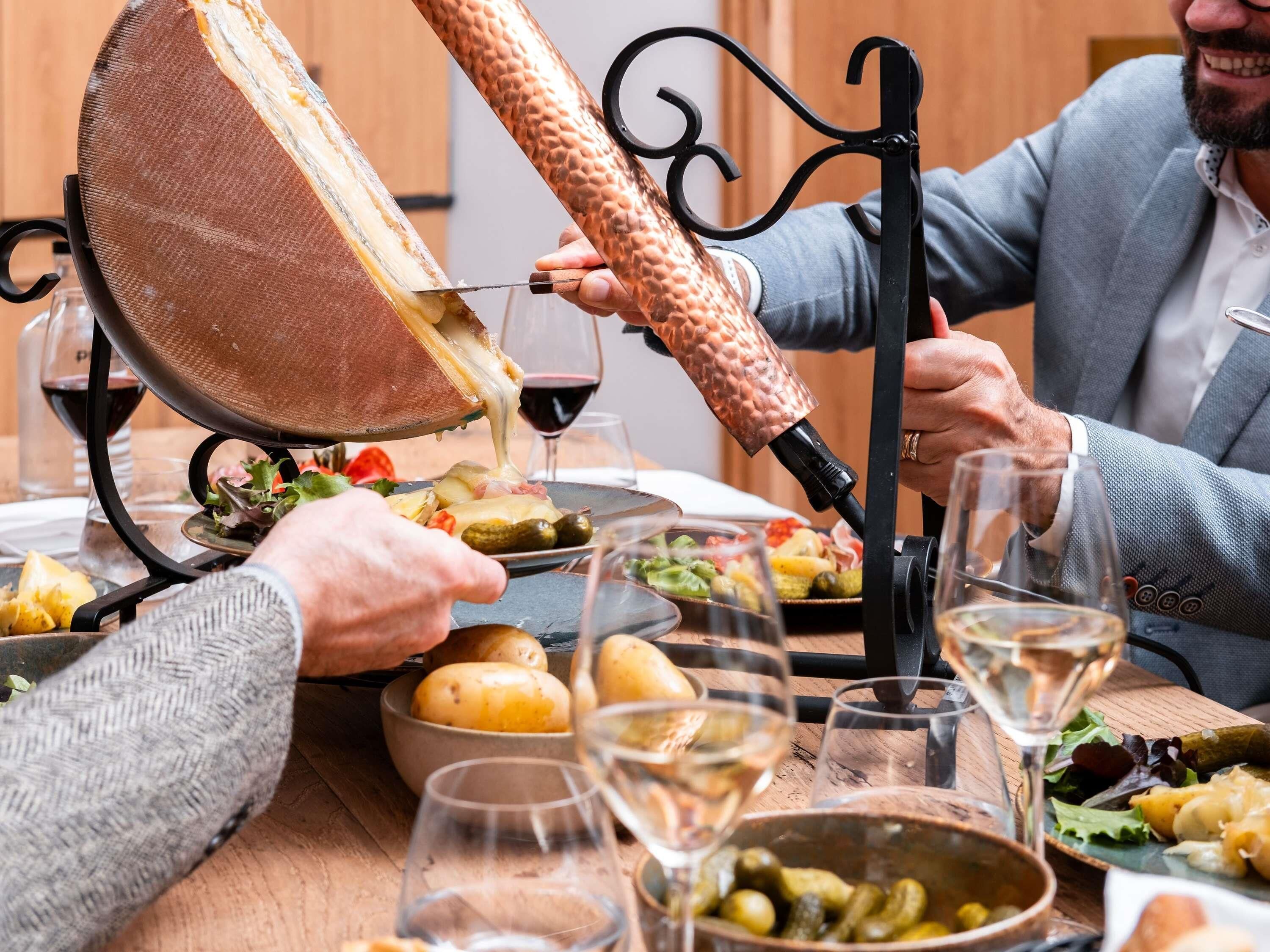 Una mesa de comedor con una variedad de platos, incluyendo una tabla de quesos, verduras y una botella de vino.
