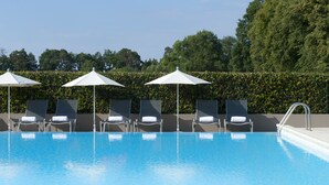 A swimming pool with lounge chairs and umbrellas, surrounded by a hedge and trees. - Mercure Chantilly Resort & Conventions (Vineuil-Saint-Firmin)