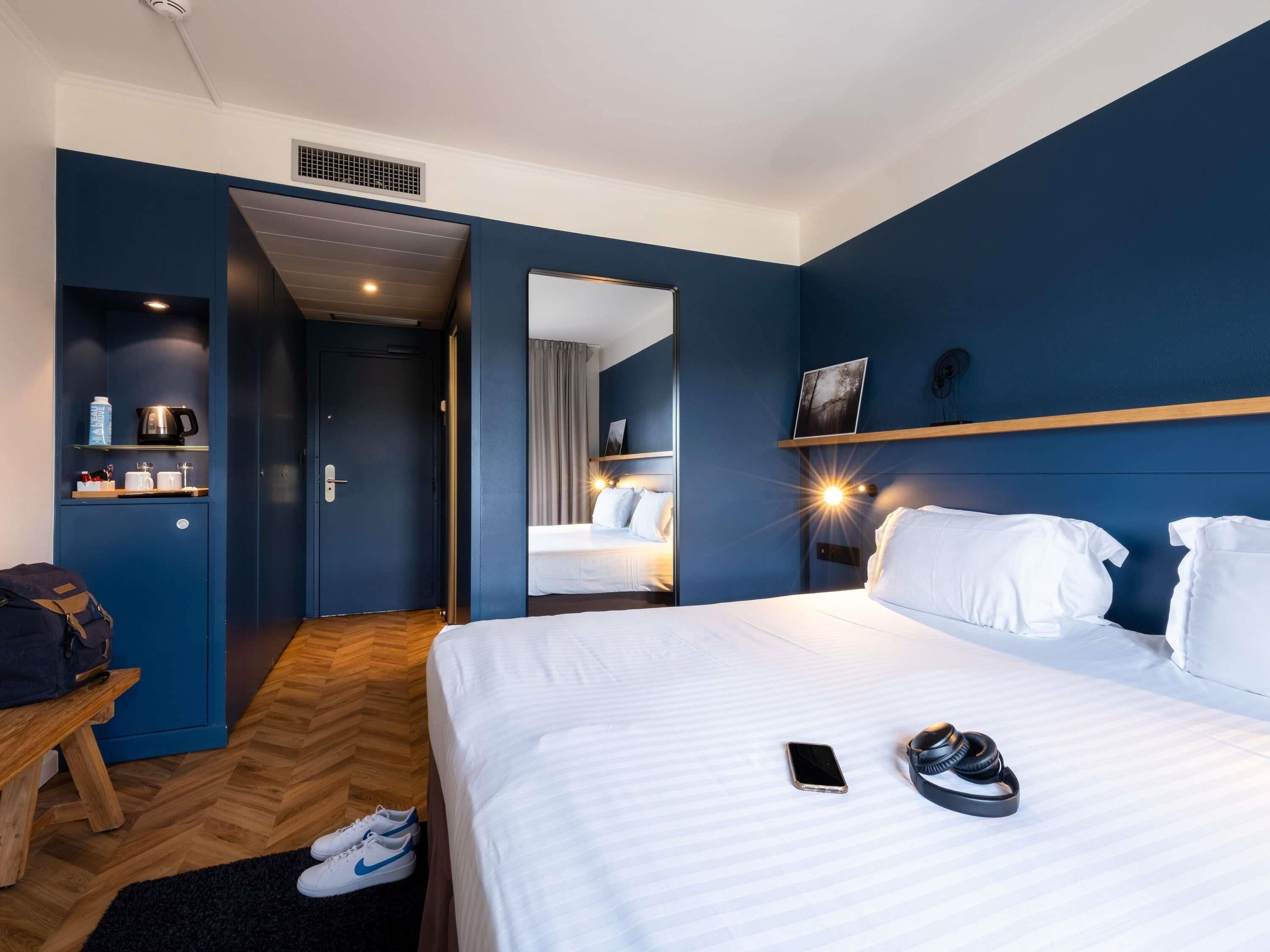 Een hotelkamer met een bed, nachtkastje, spiegel, kledingkast en een zithoek.