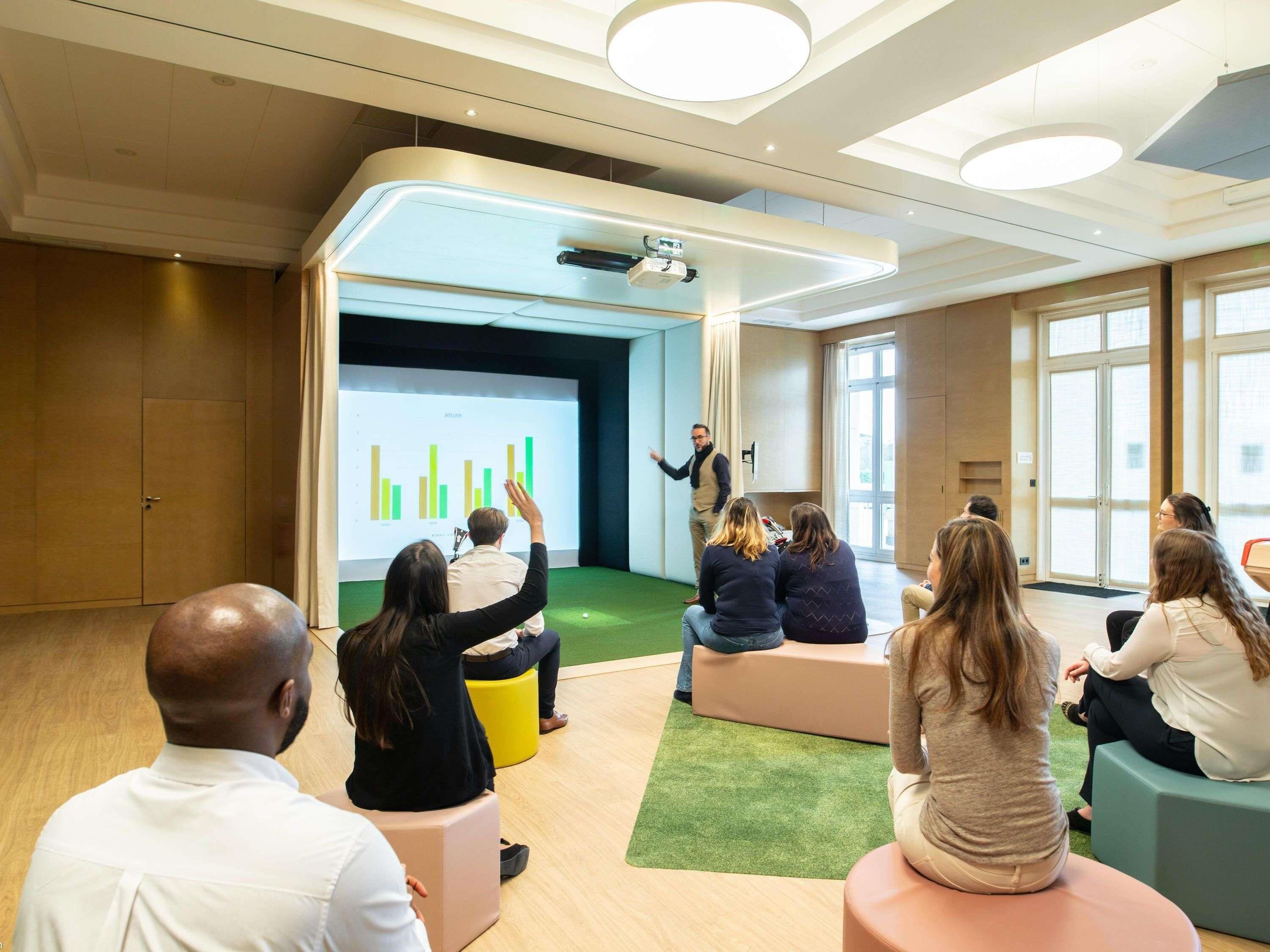 A modern conference room with a presentation screen, green carpet, and a speaker.