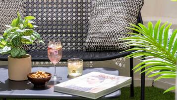 A wicker sofa with patterned cushions, a small table with a potted plant, a bowl of snacks, and two glasses of a pink beverage.
