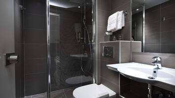 A modern bathroom with a glass-enclosed shower, a white toilet, and a sink with a mirror above it.