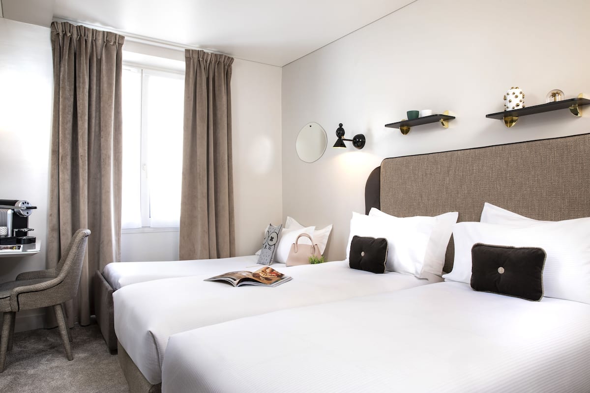 A hotel room with two beds, a desk with a coffee machine, and a window with curtains.