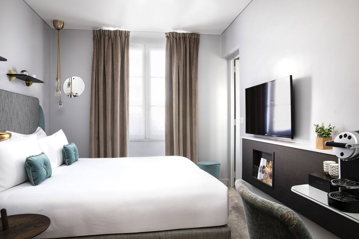 A modern hotel room with a large bed, a flat-screen TV, a fireplace, and a view of the outdoors.