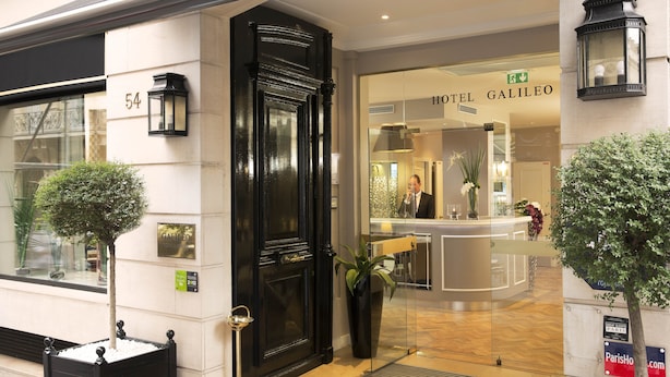 Een hotelentree met een zwarte deur, een receptiebalie en een bord met Hotel Galileo.