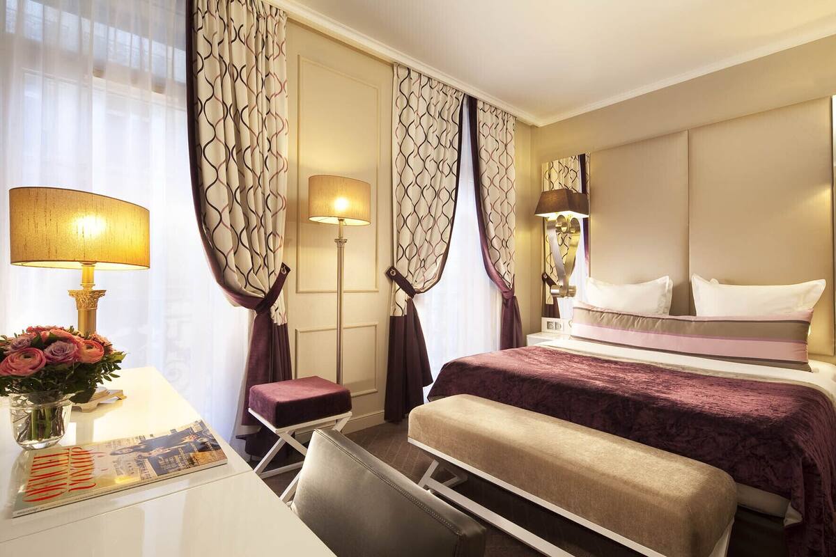 A hotel room with a bed, bedside tables, a desk, and a chair.
