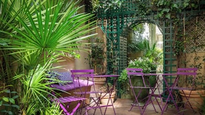 Een patio in een tuin met paars meubilair, een groene lierbogen en potplanten.