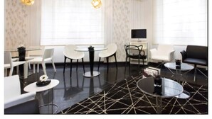 Una sala de estar moderna con una mesa de centro de vidrio, sillas blancas, un sofá negro y un televisor sobre un mueble.