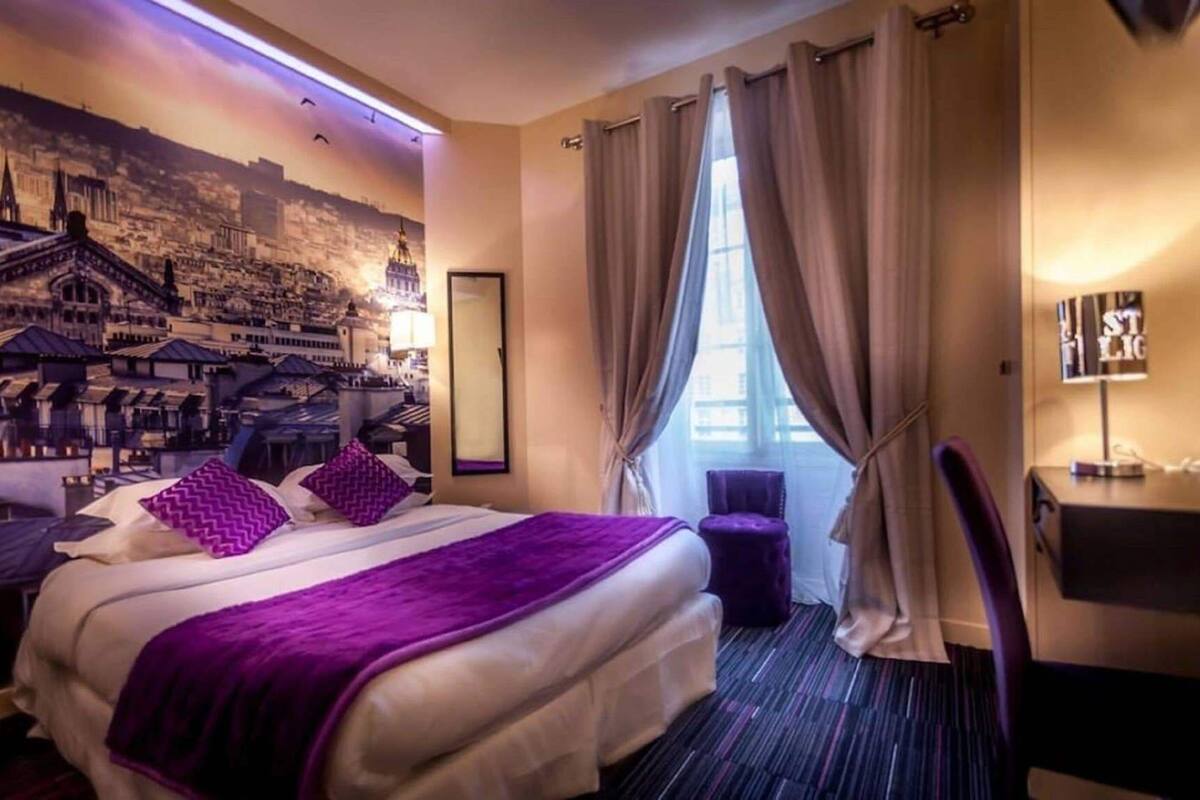 Habitación de hotel con una cama grande, un escritorio, una silla y un mural con vistas a la ciudad.