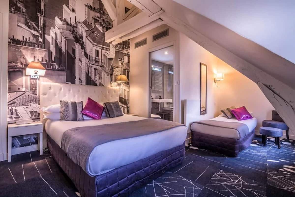 Un dormitorio con una cama grande, un sofá más pequeño, una mesita de noche y una lámpara de pared.