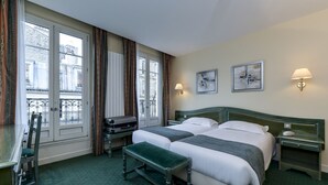 Een hotelkamer met twee bedden, een bureau, een bankje en een raam met gordijnen.