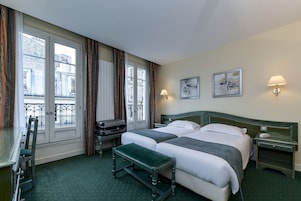 Habitación de hotel con dos camas, un escritorio, una banca y una ventana con cortinas.