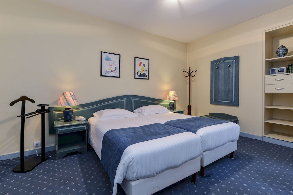 A double bed with a blue headboard, two bedside tables with lamps, a coat rack, and a shelf with decorative items.