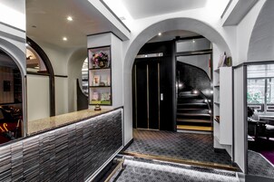 Vestíbulo de hotel con recepción, escalera y vista al exterior.