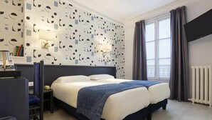 A hotel room with a large bed, a desk with a chair, a bookshelf, and a window with curtains. - Résidence du Pré (Paris)