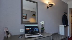 A laptop on a desk with a mirror above it, a small potted plant, and a coat rack with a jacket. - Résidence du Pré (Paris)