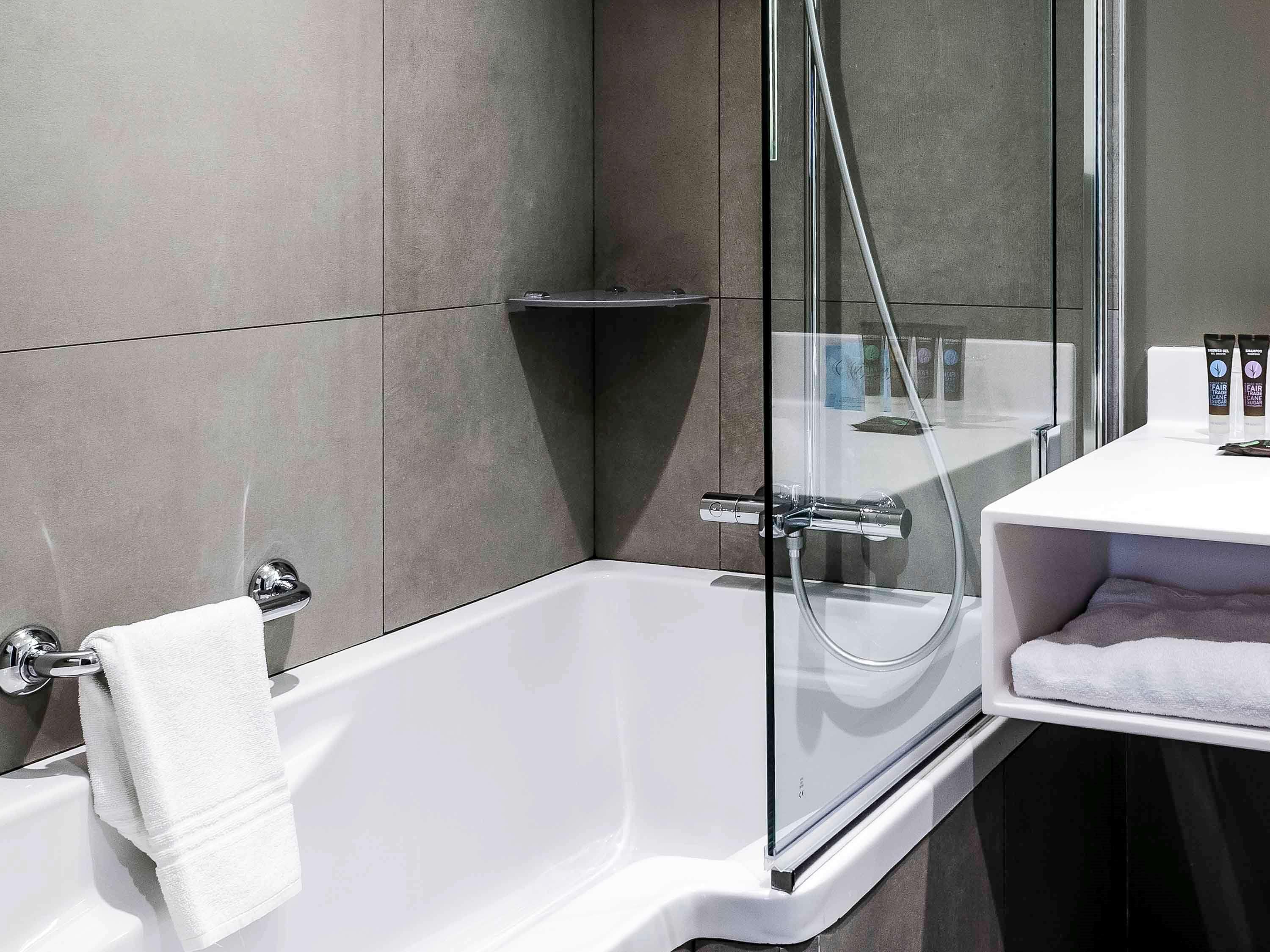Un baño moderno con ducha de vidrio, una bañera blanca y un lavamanos blanco con una toalla.
