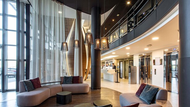 Eine geräumige Lobby mit einer gebogenen Sitzecke, einem Empfangstresen und einer modernen Treppe.