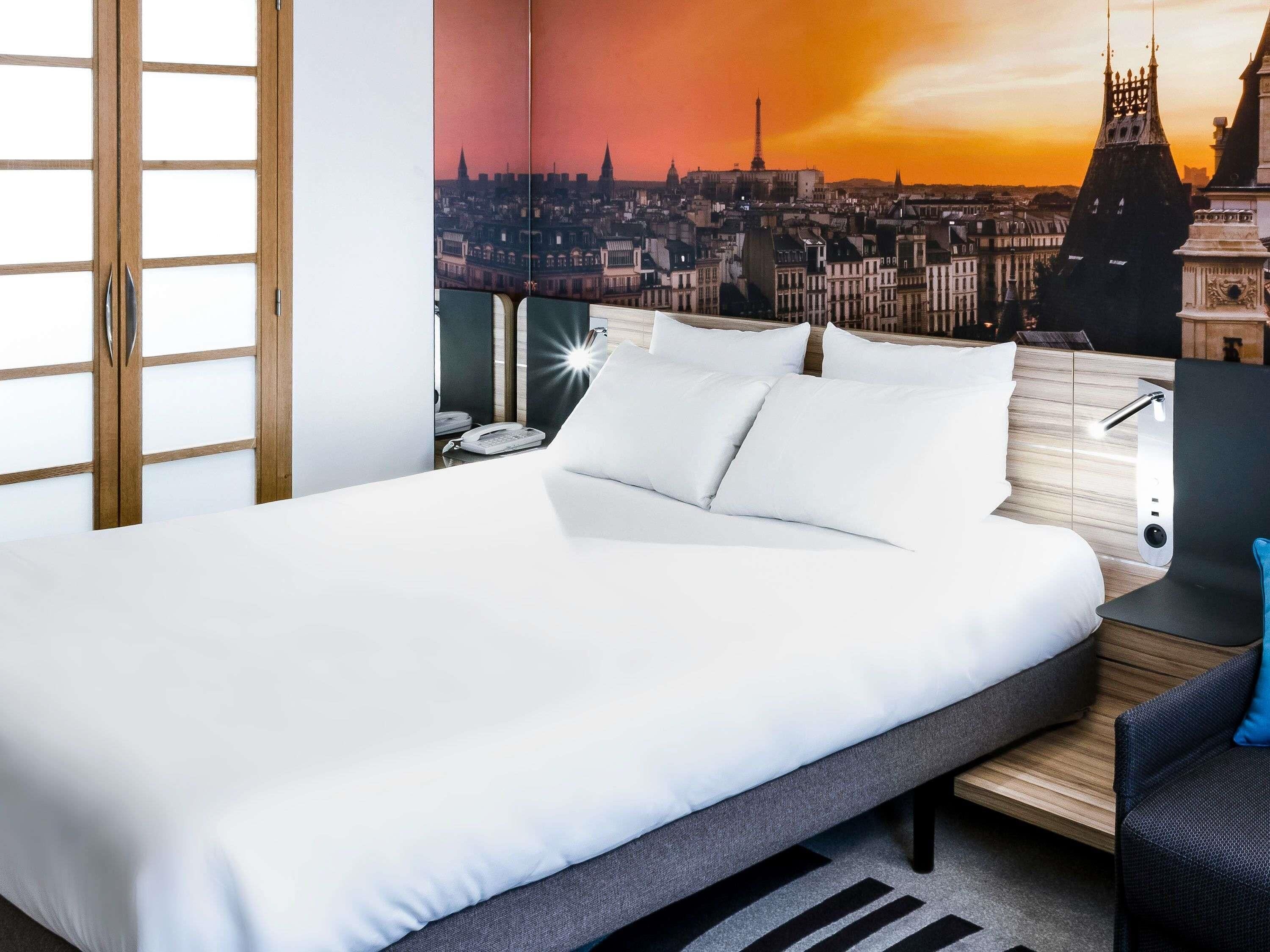 A hotel room with a bed, a desk with a phone, and a cityscape view.