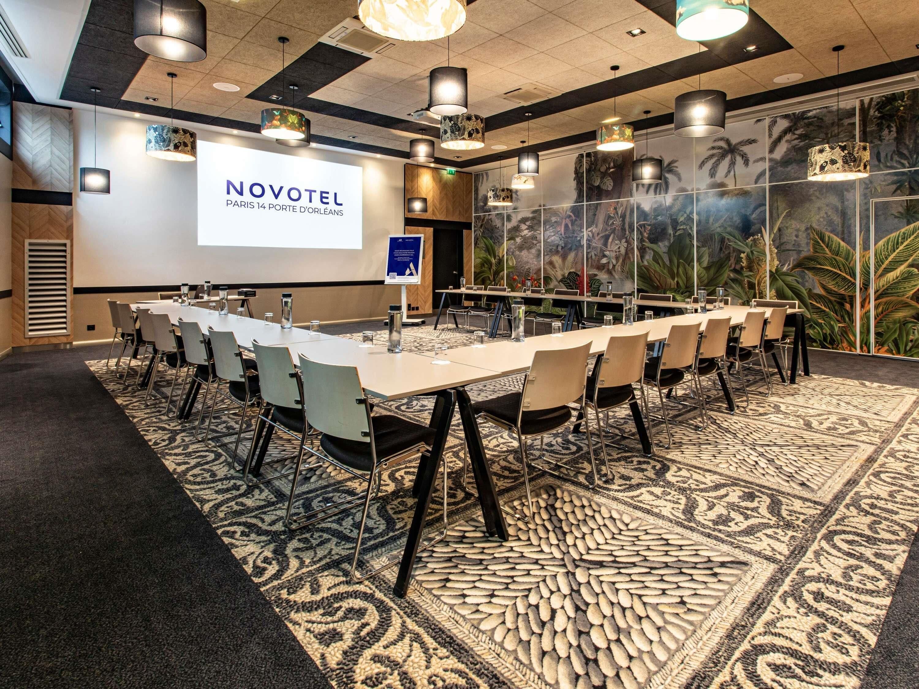 A conference room with a long table, chairs, a projector screen, and a tropical mural.