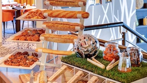 Ein Frühstücksbuffet mit verschiedenen Backwaren und Brot auf Etageren, eine Glaskaraffe mit Gewürzen und ein kleiner Topf mit Pflanze auf einem Tisch.