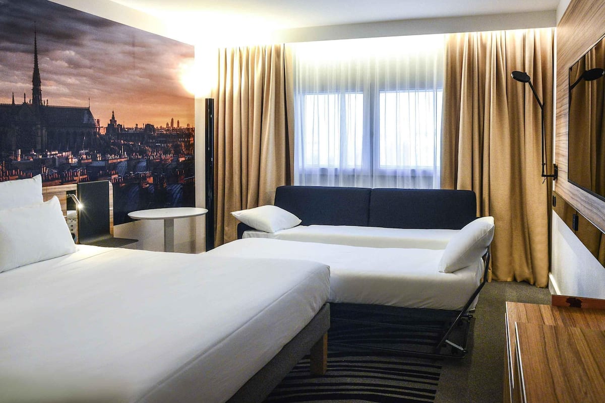 Une chambre d’hôtel avec deux lits, une vue sur la ville, une petite table et un miroir.