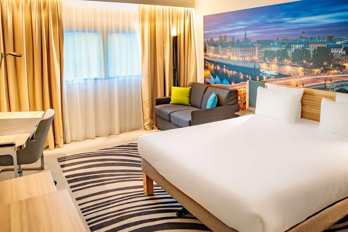 Une chambre d’hôtel avec un grand lit, un canapé, un bureau et une vue sur le paysage urbain.