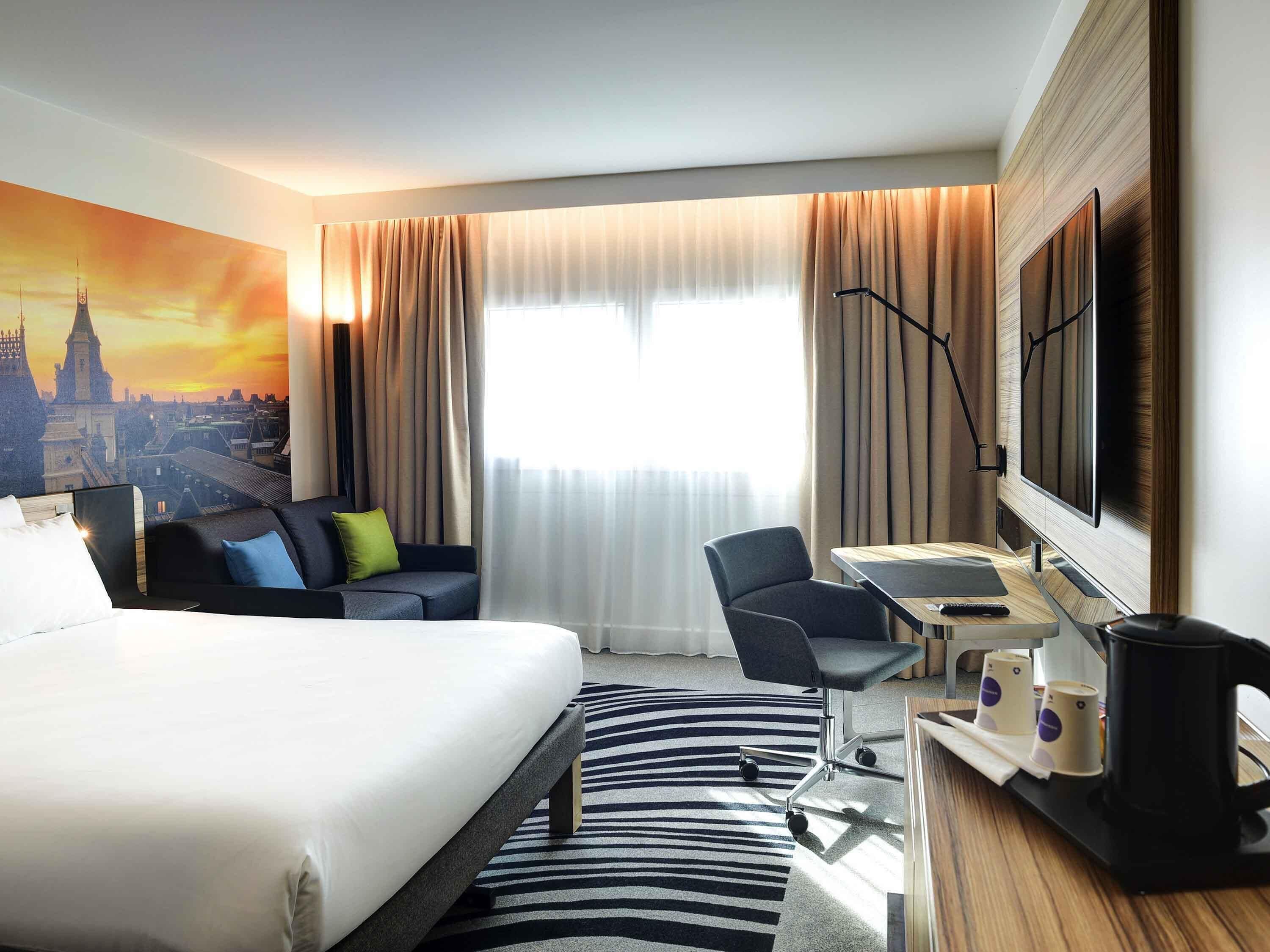 A hotel room with a bed, a desk with a chair, a coffee maker, and a TV.