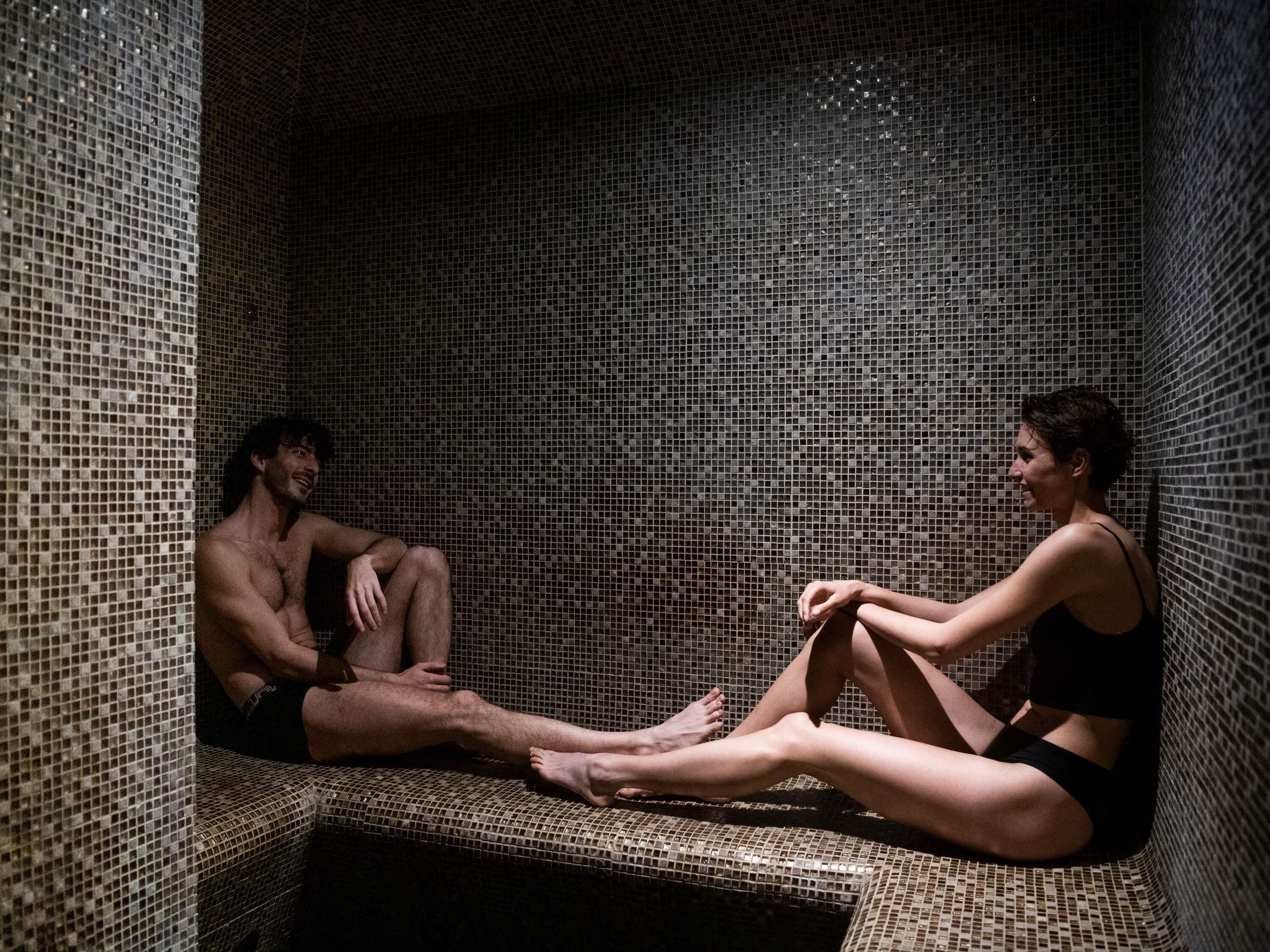 A small, tiled room with a bench and a person sitting on it.