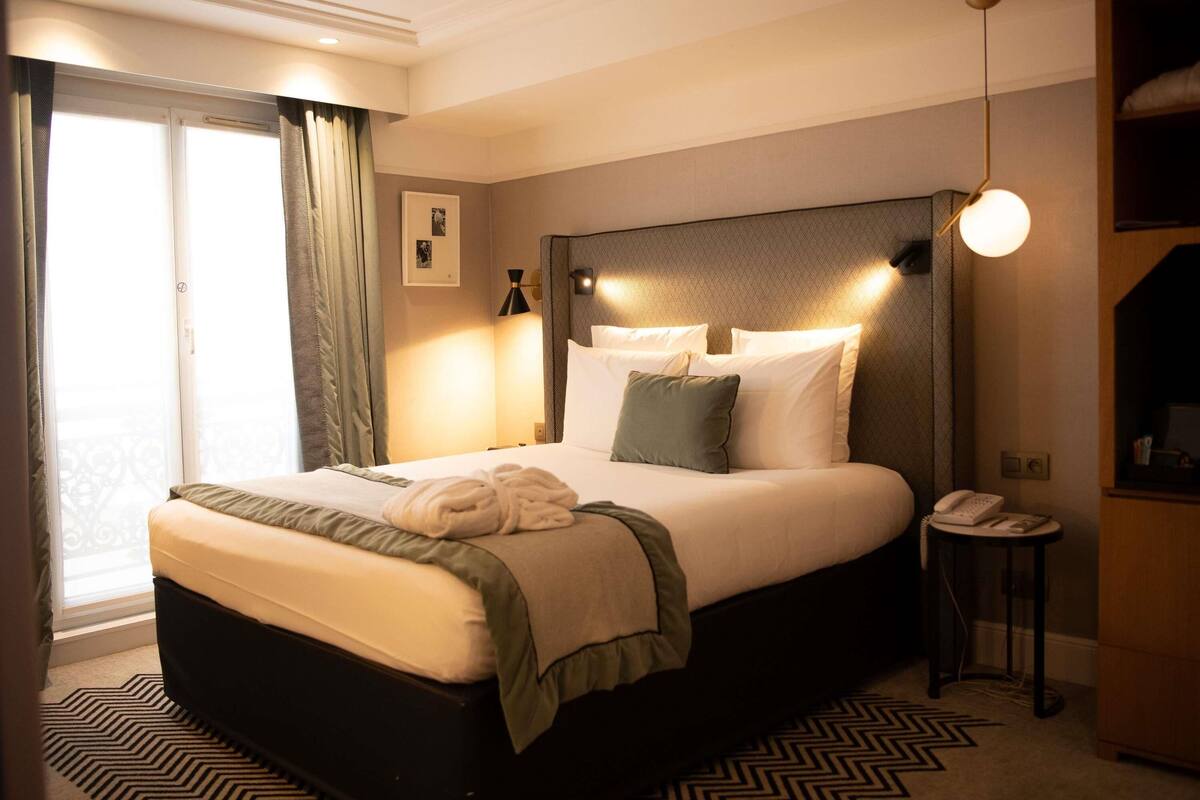 A hotel room with a large bed, a bedside telephone, a lamp, and a view of the outside through a sliding door.